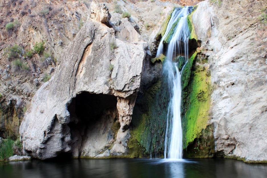 A long exposure photo of Paradise Falls in Thousand Oaks; a thin waterfall dropping into a pool alongside a large rock outcropping.
