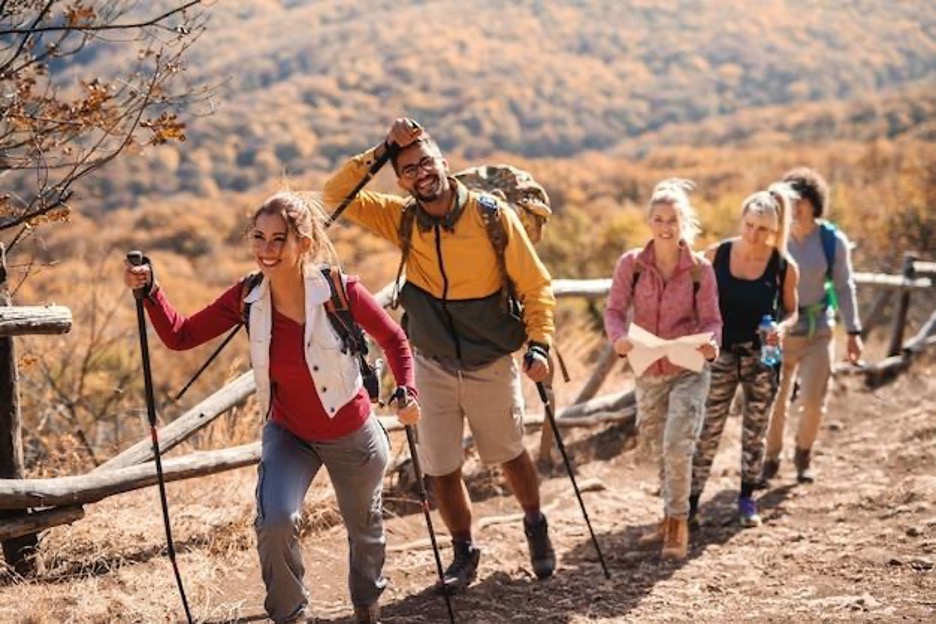 A group of five happy hikers walking uphill on a trail in Thousand Oaks, CA, with fall foliage visible in the background.