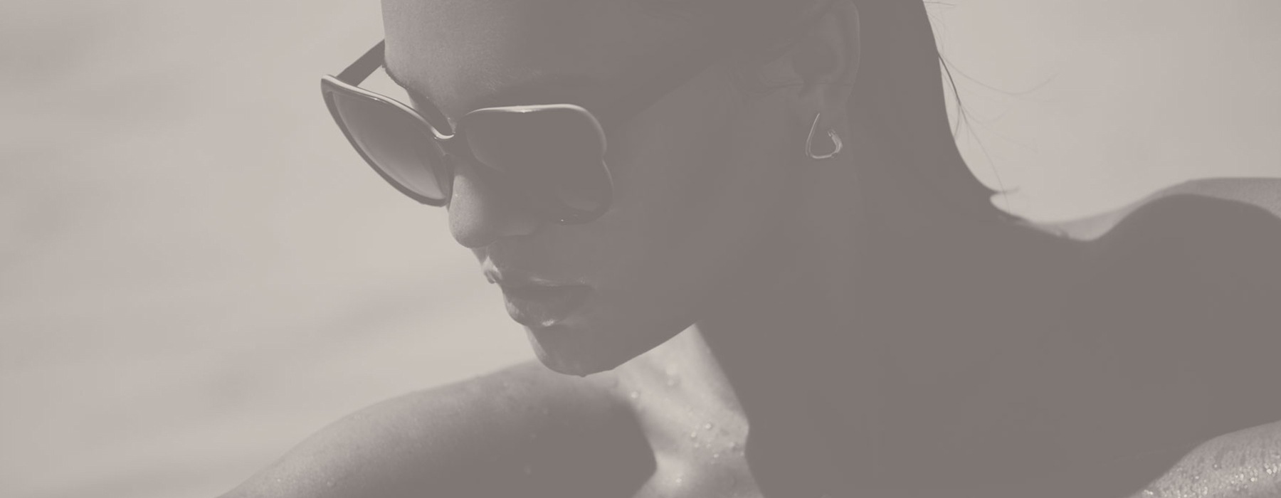 lifestyle image of a young woman looking down in sunglasses from within a pool