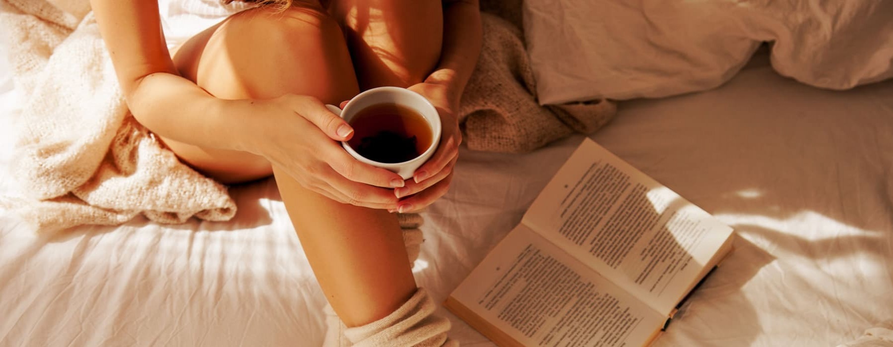 lifestyle image of a person holding a cup of coffee in bed