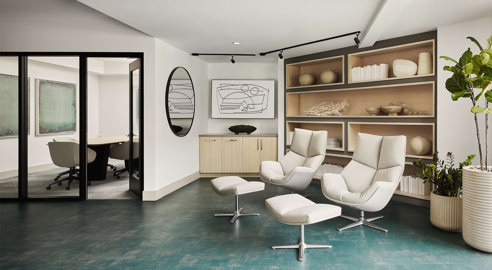 A serene lounge with white recliners, ottomans, built-in shelves, and glass-walled meeting rooms at Santal Thousand Oaks.