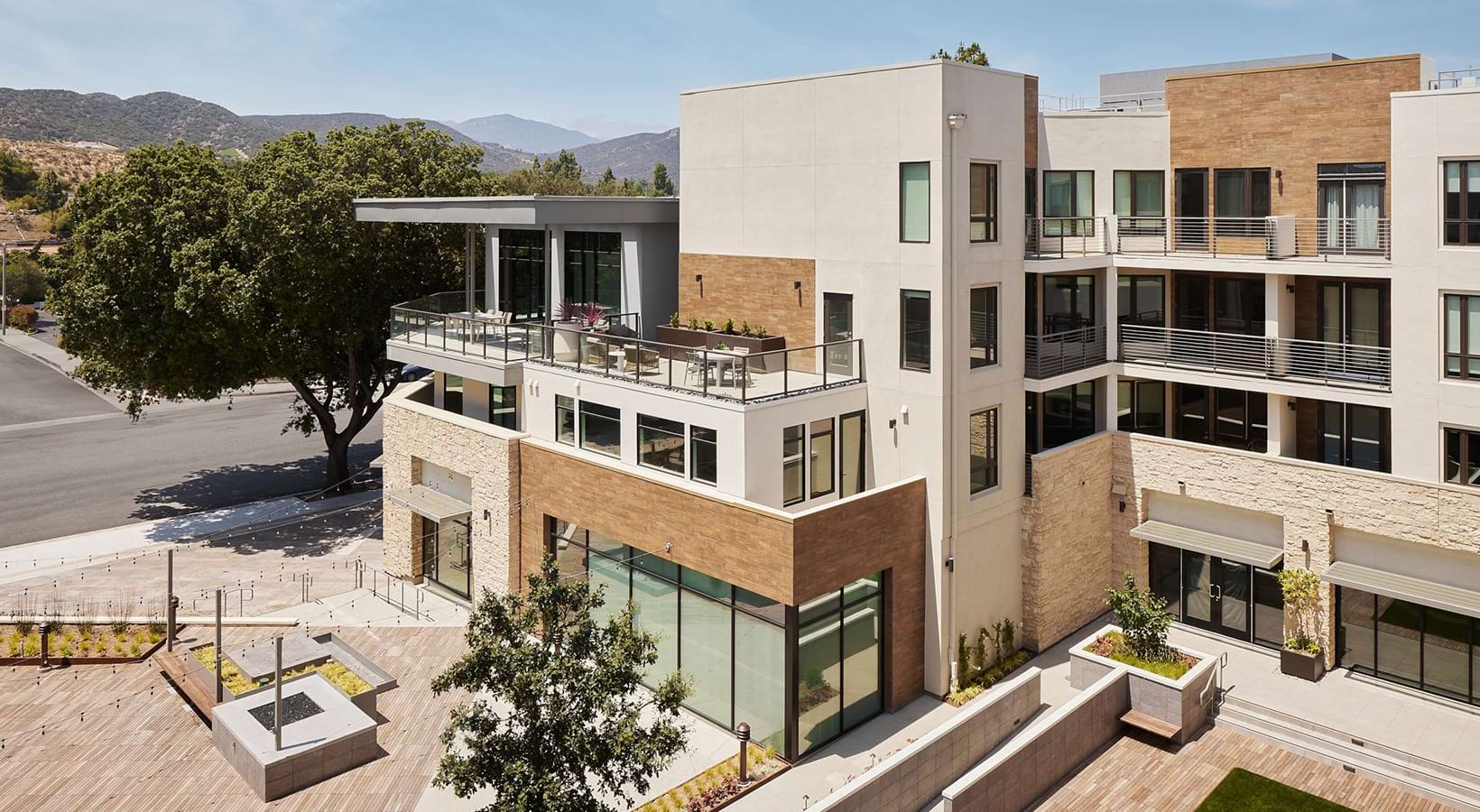 A modern building featuring glass balconies and outdoor seating areas above a paved courtyard at Santal Thousand Oaks.